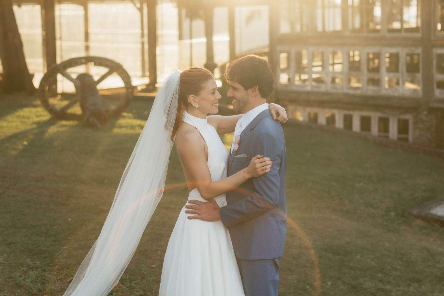 A couple shares a romantic moment at sunset in their wedding attire on a grassy terrain.