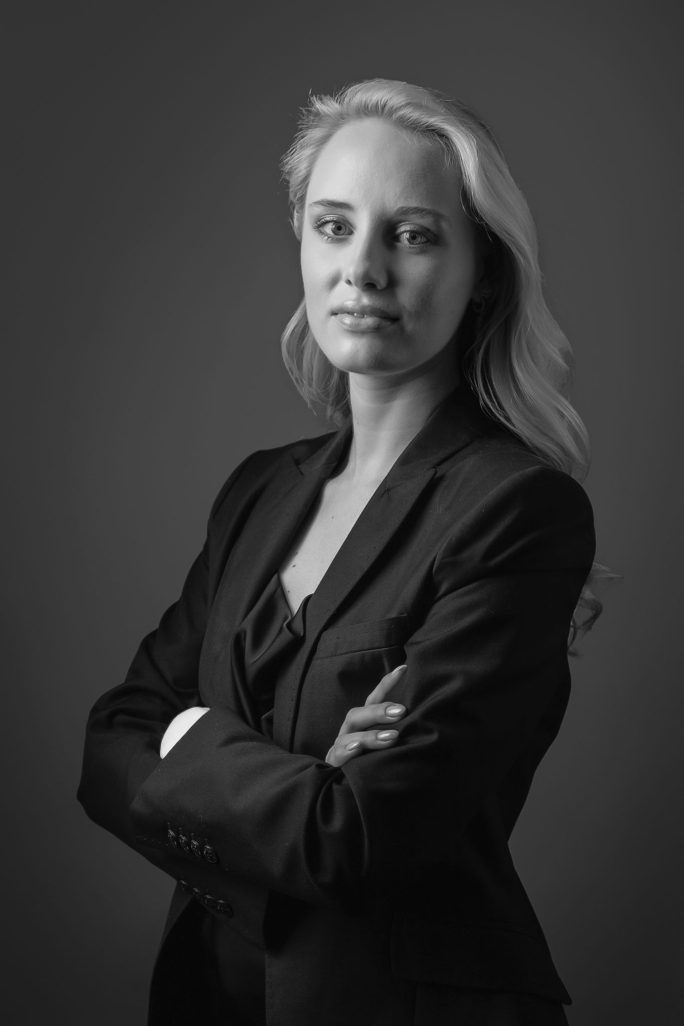 Professional black and white portrait of a person in a business suit with crossed arms against dark background.