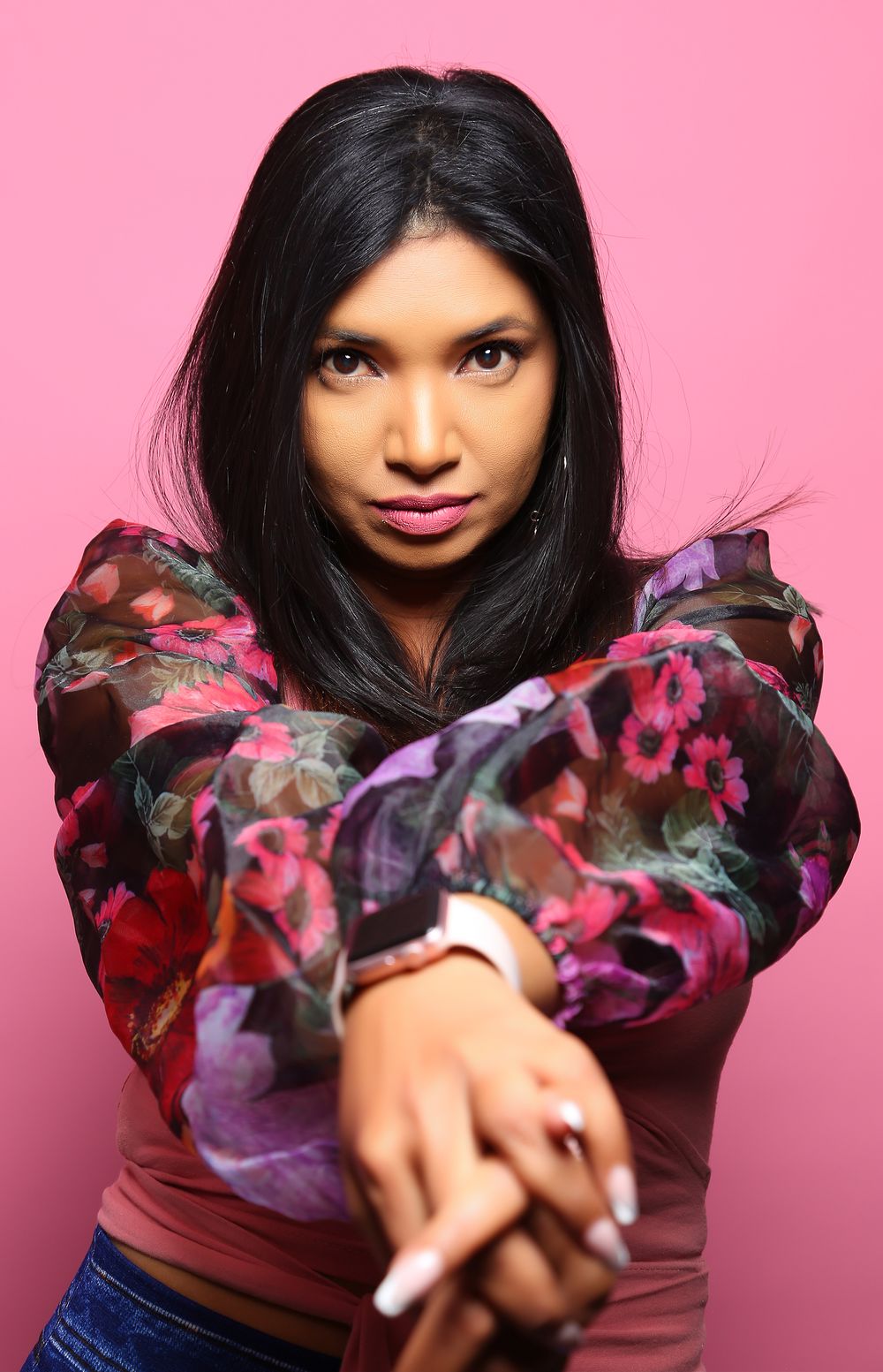 A person in a floral print top gazes confidently at the camera against a pink background.