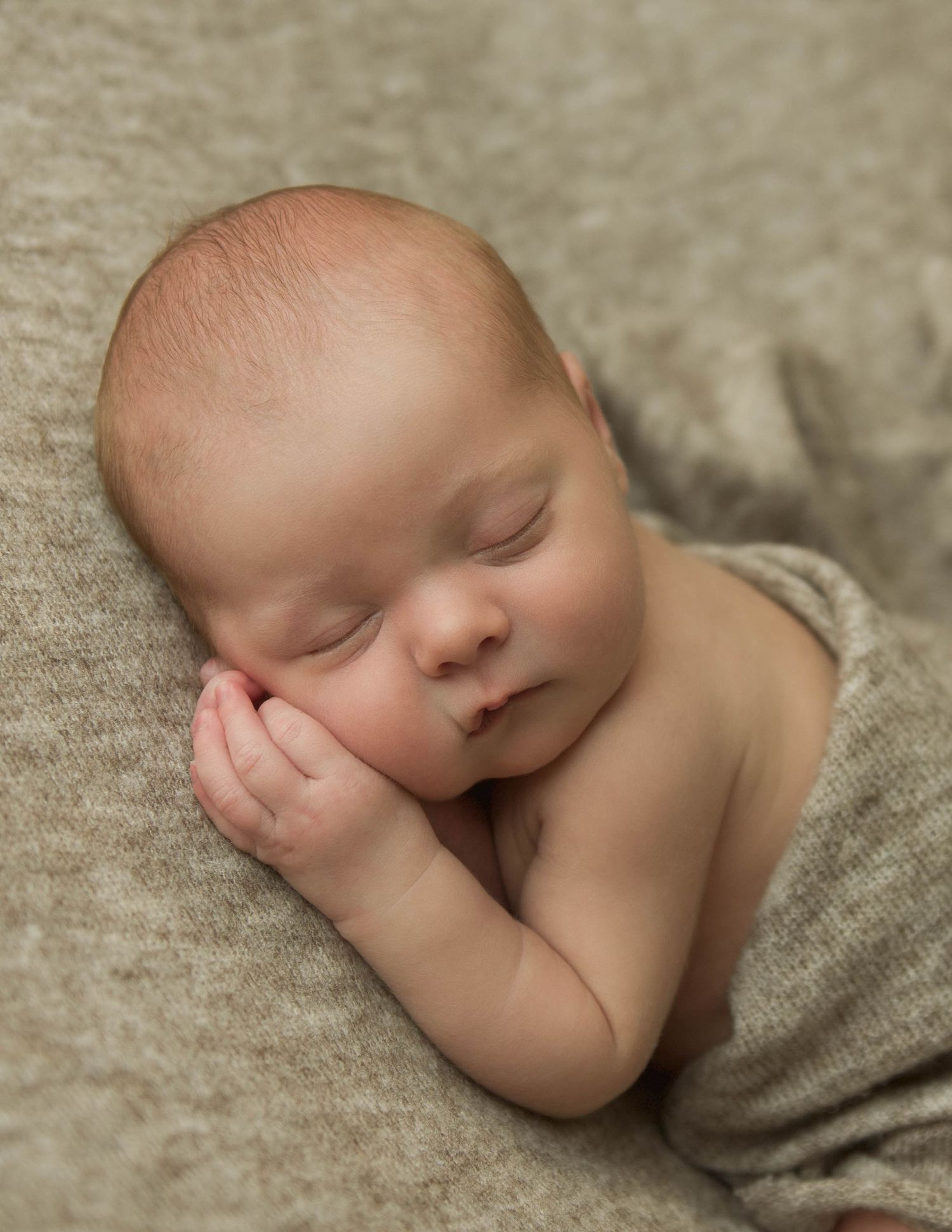 Peaceful sleeping newborn baby photographed in soft gray tones on textured fabric.