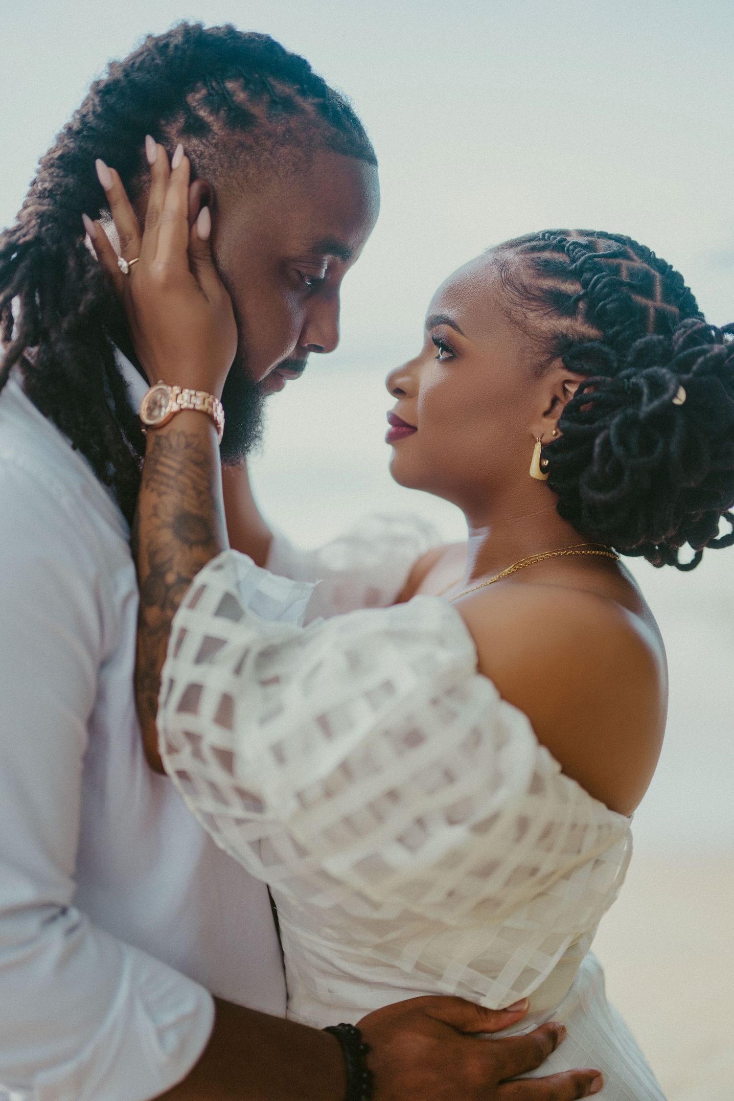 Two people share an emotional moment in white wedding attire during an outdoor beach ceremony.