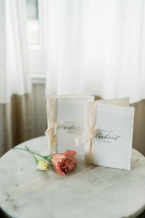 White place cards with handwritten calligraphy on marble table with delicate pink roses for elegant wedding reception.