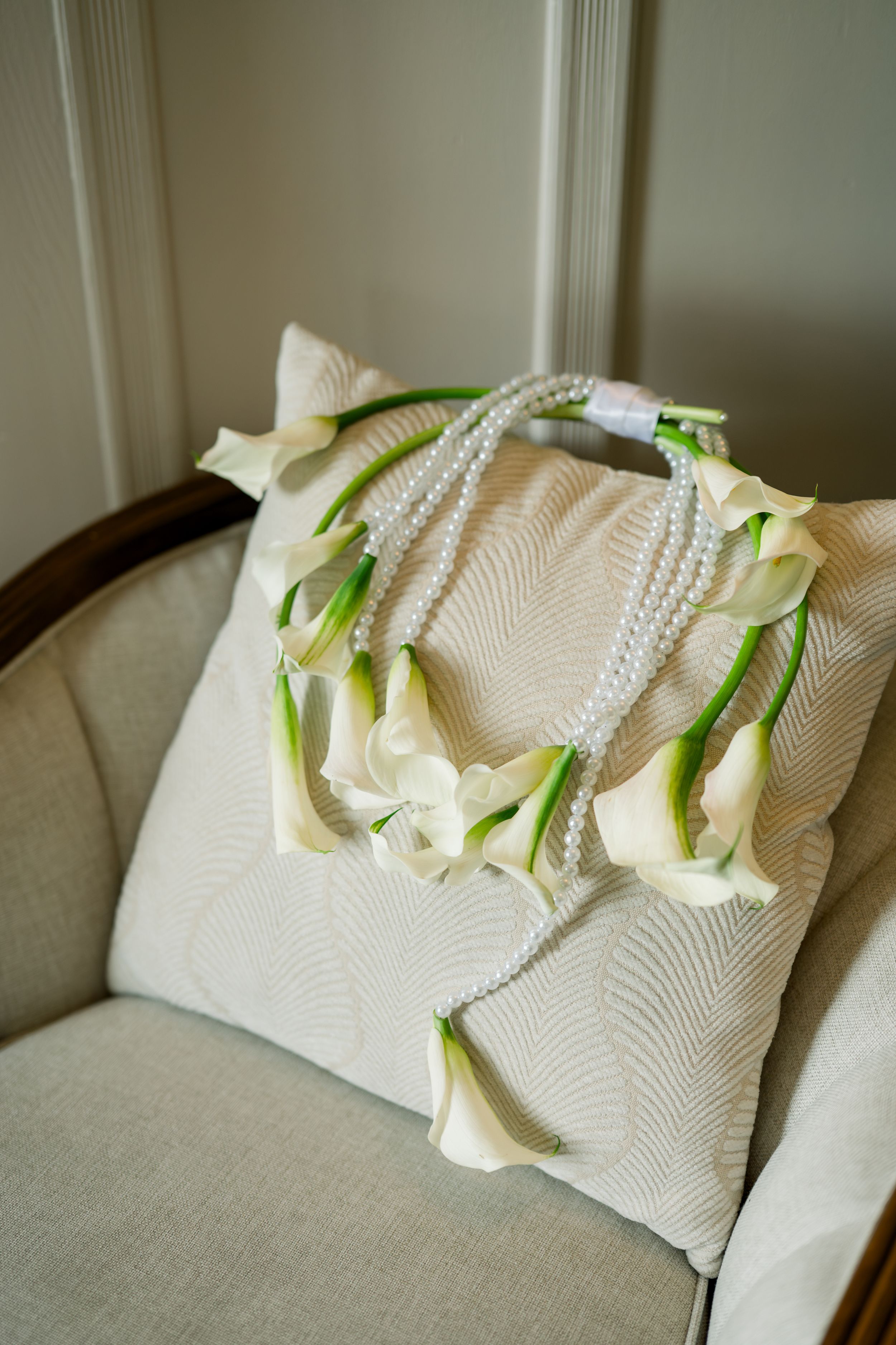 White floral lei with pearls displayed on cream textured cushion.