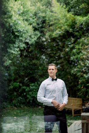 Classic formal attire with white dress shirt and bow tie against lush garden backdrop with wooden bench.