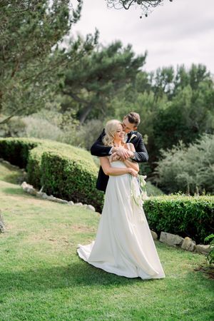 A romantic wedding moment captured on manicured green lawn surrounded by elegant hedges and pine trees.