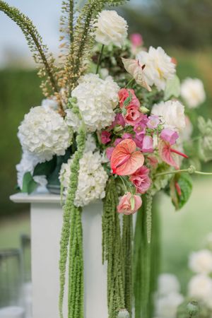 Elegant floral arrangement featuring white hydrangeas, pink anthurium flowers and cascading green amaranth for a wedding.