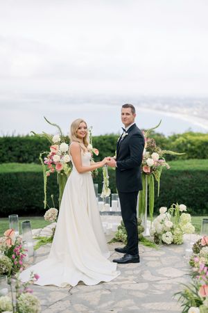 A beautiful outdoor wedding ceremony on a stone patio decorated with pink and white floral arrangements and greenery.