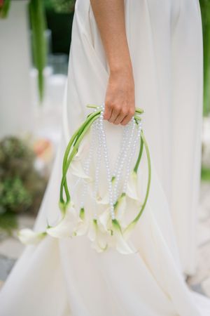 A delicate pearl and white calla lily wedding bouquet hangs elegantly against a flowing white wedding dress.