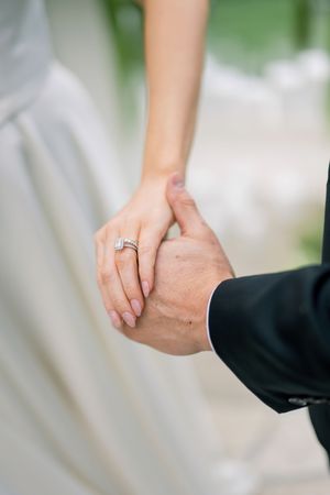 Close-up of newlywed couple holding hands and showing engagement ring against blurred background.