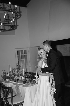 A romantic black and white wedding reception scene with a couple dancing near an elegantly decorated dining table.