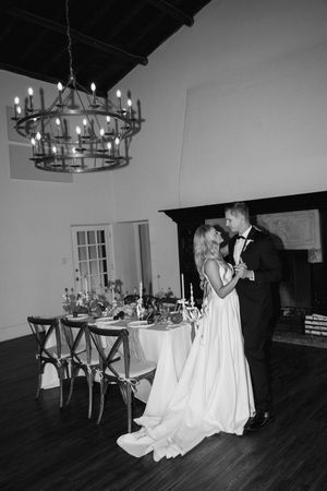 A couple shares their first dance in an elegant reception venue with a rustic chandelier and formal table setting.