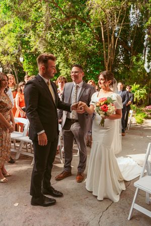 An outdoor garden wedding ceremony with guests gathered around as couple stands at the altar under lush greenery.