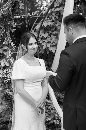 Black and white photo of wedding ceremony under garden arch with ivy and white draping.