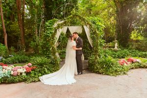 A couple shares an intimate moment under a floral arch during their garden wedding ceremony.