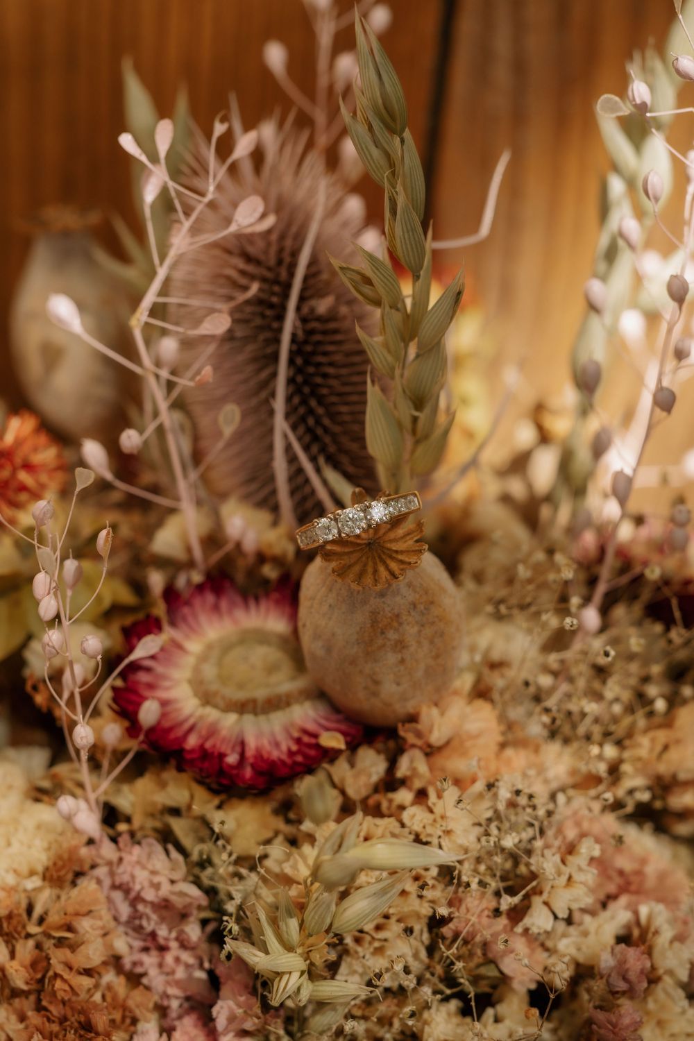 A diamond engagement ring perched delicately on dried flowers and pods in a rustic bohemian arrangement.