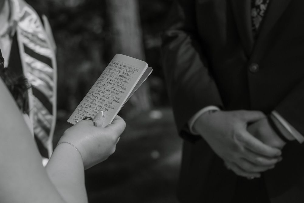 A black and white photo shows hands holding papers during what appears to be a wedding ceremony or formal event.