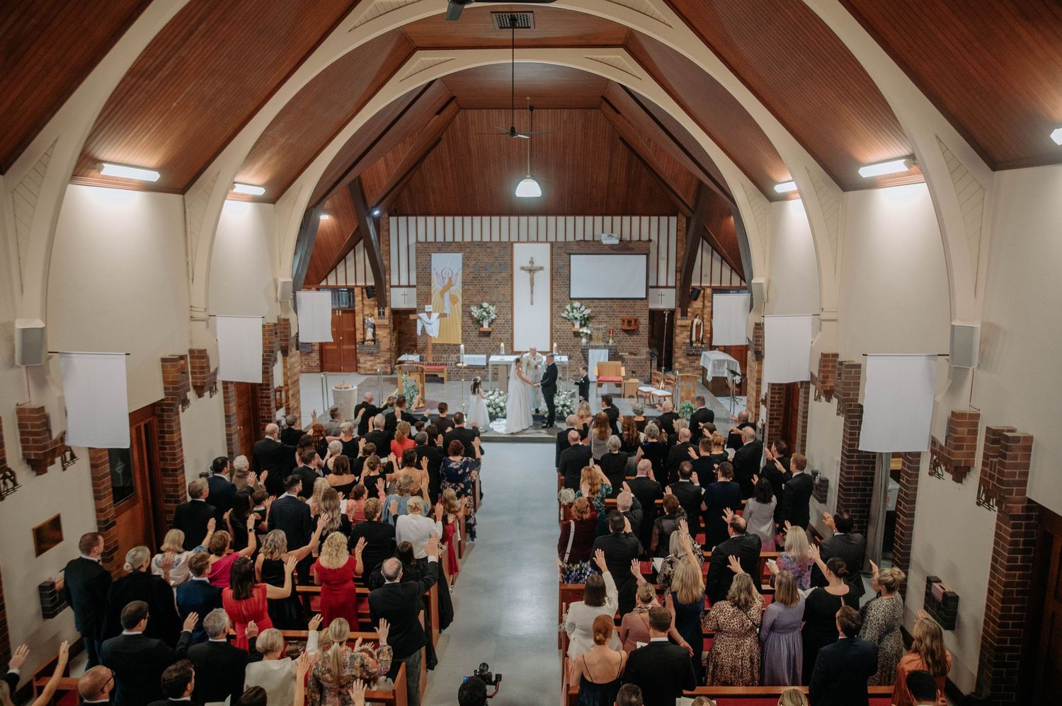 High angle view of a wedding ceremony taking place inside a church with wooden beams and vaulted ceiling.