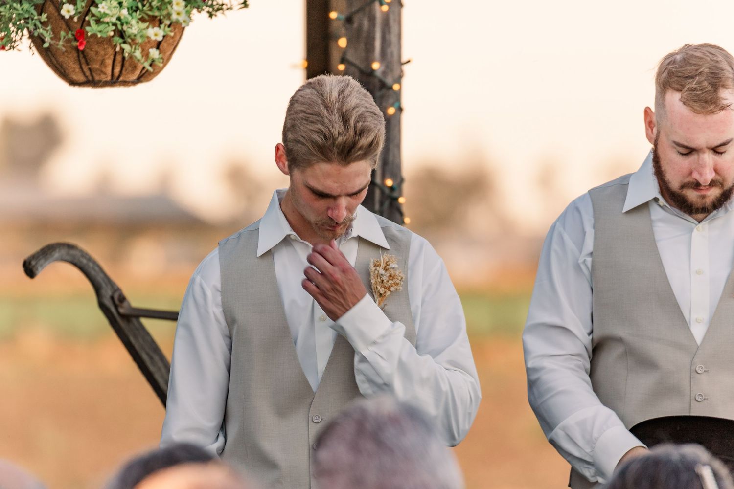 Two members of a wedding party share an emotional moment during an outdoor ceremony at sunset.