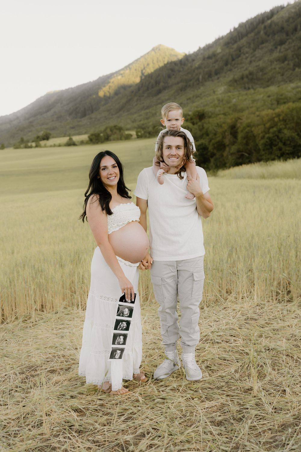 A family maternity photo shoot in a mountain meadow with a strip of sonogram images.