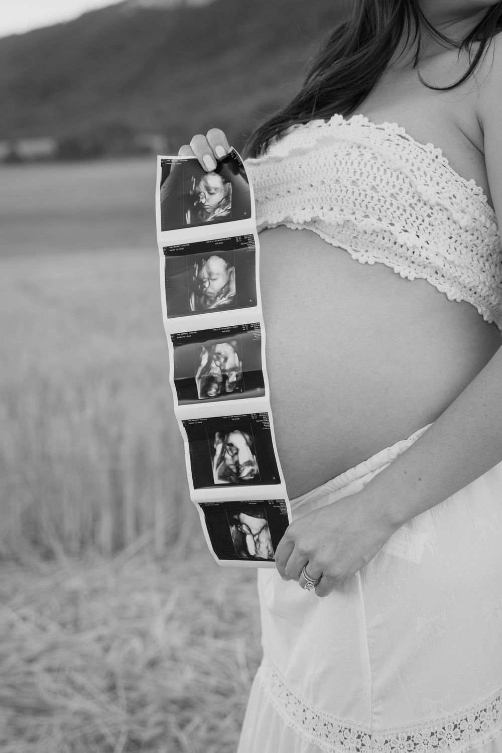 A strip of ultrasound photos displayed against a pregnant belly in a black and white photograph.