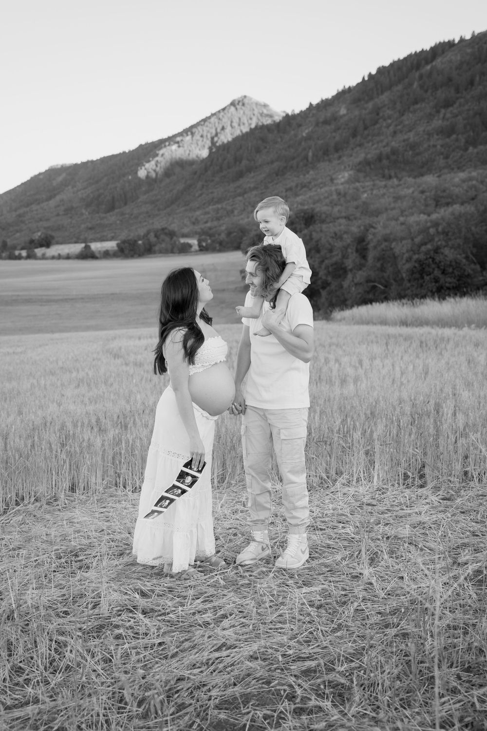 Family photoshoot in black and white showing playful interactions in a mountain field.