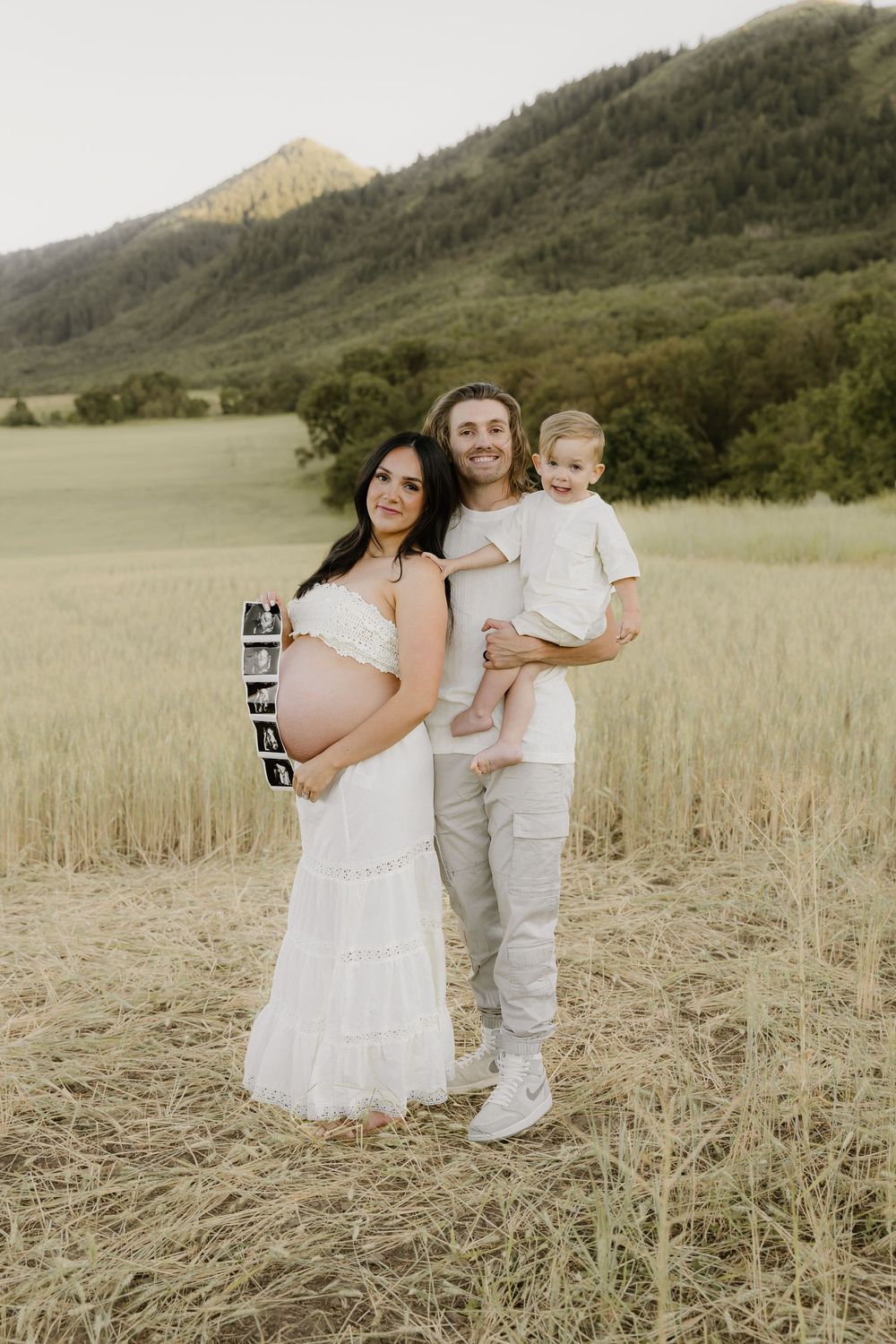 A family poses together in a field with mountains visible in the background.
