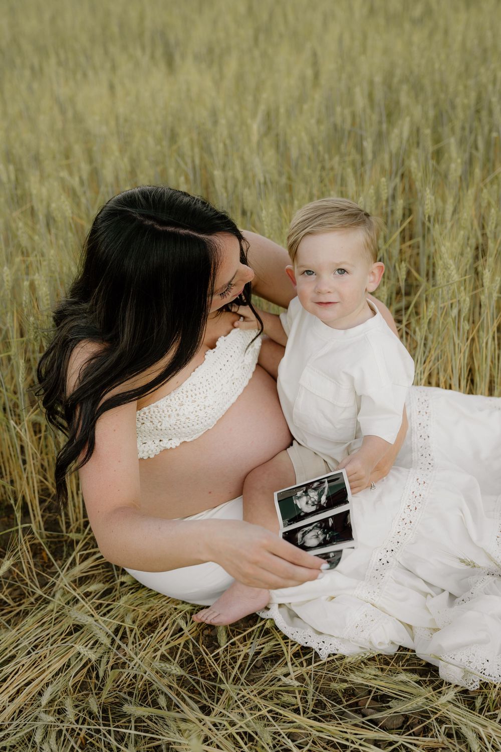 Mother-to-be and child look at ultrasound photos in wheat field.