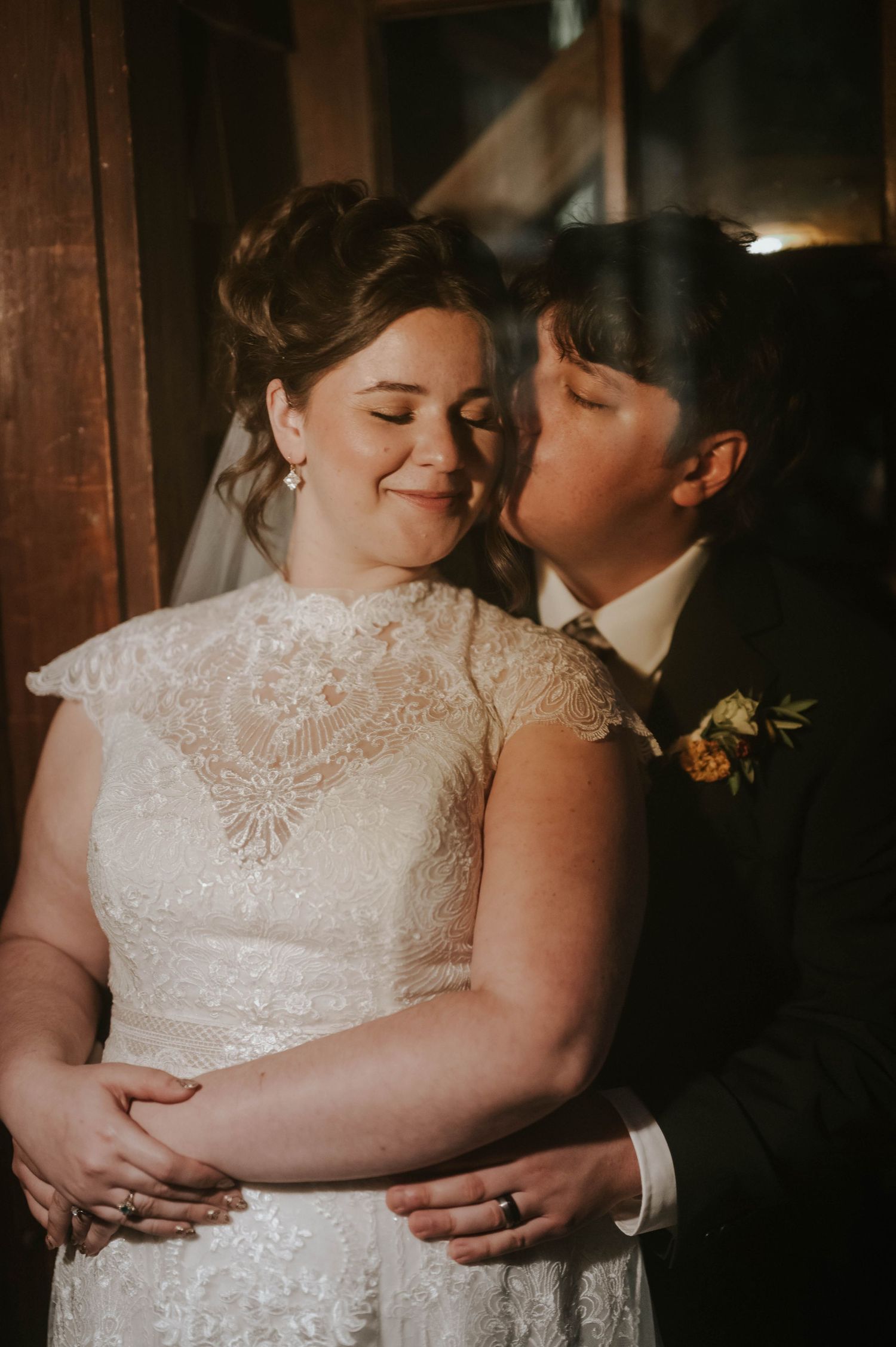 Intimate wedding moment captured in warm, moody lighting with lace dress details.