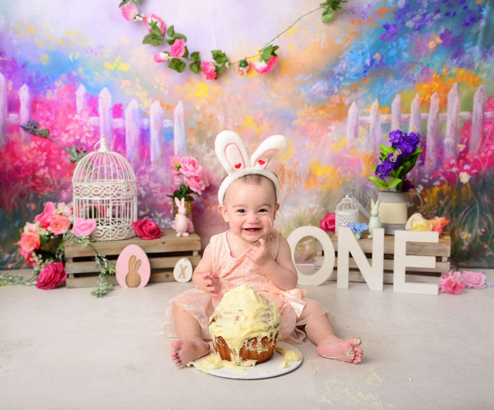 Smiling baby girl in bunny ears enjoying Easter-themed first birthday cake smash with floral backdrop. portrait in the Macarthur region