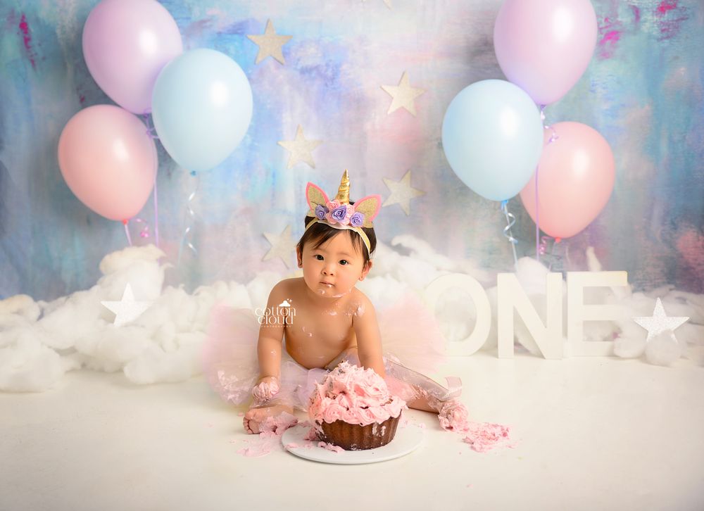 Baby girl in unicorn headband and tutu with giant cupcake for first birthday cake smash portrait in the Macarthur region by Cotton Cloud Pho