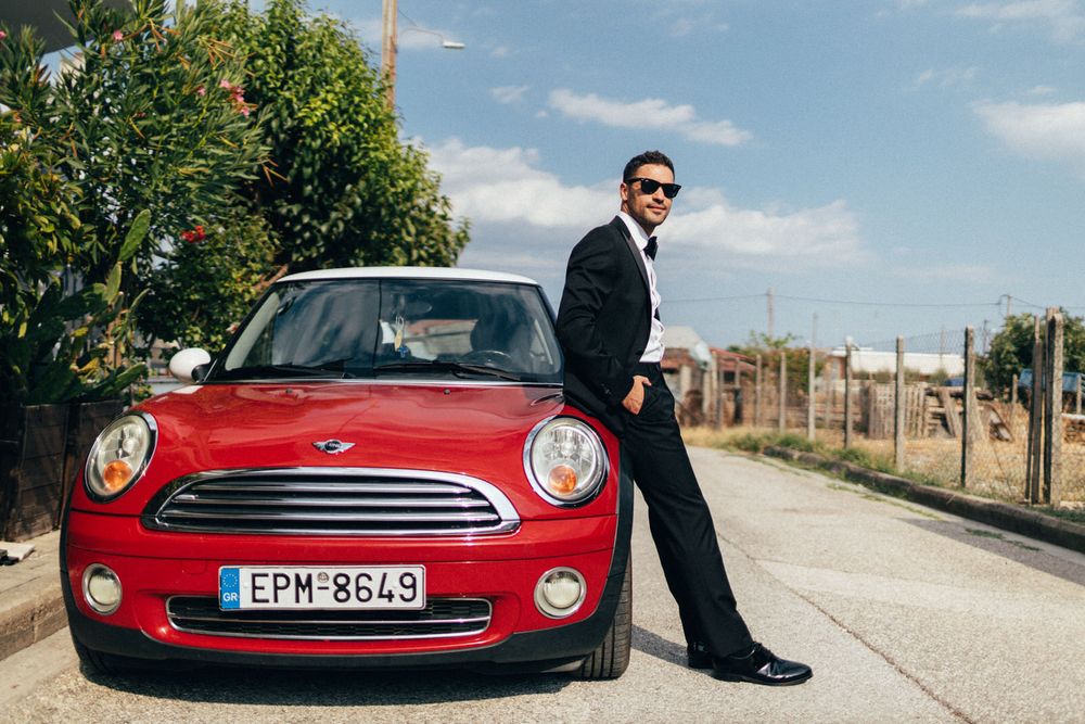 Stylish figure leaning against a red Mini Cooper on a rural road.