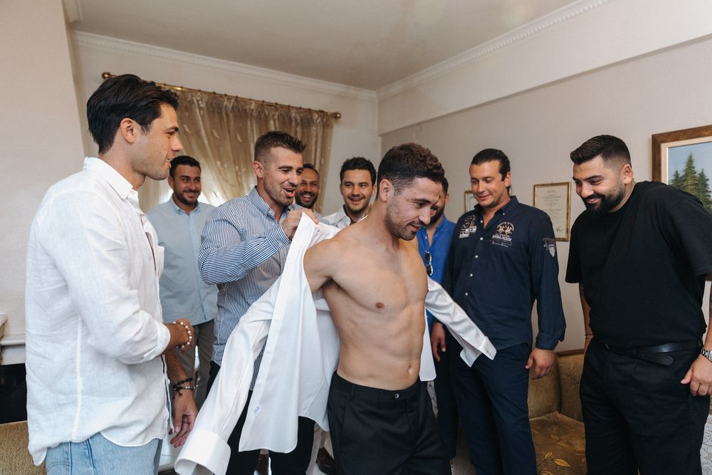 A group of groomsmen help their friend get dressed before a wedding ceremony.