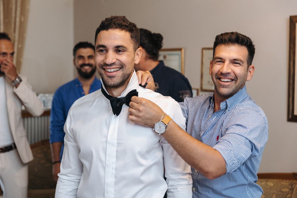 Two people adjusting a bow tie during wedding preparations.