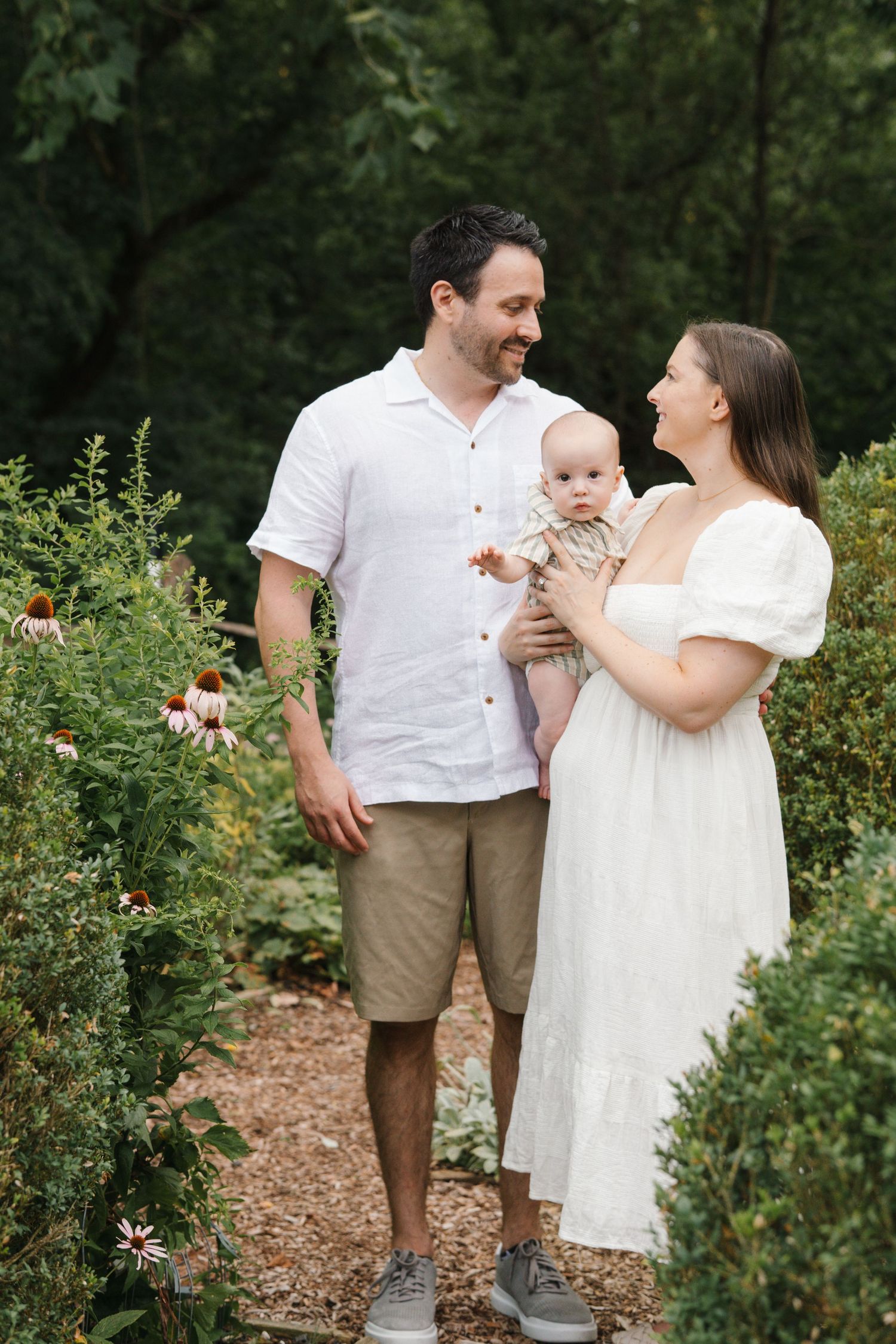 Parents standing in the lush wildflower garden at Barclay Farmstead, looking lovingly at each other while surrounded by blooming flowers.