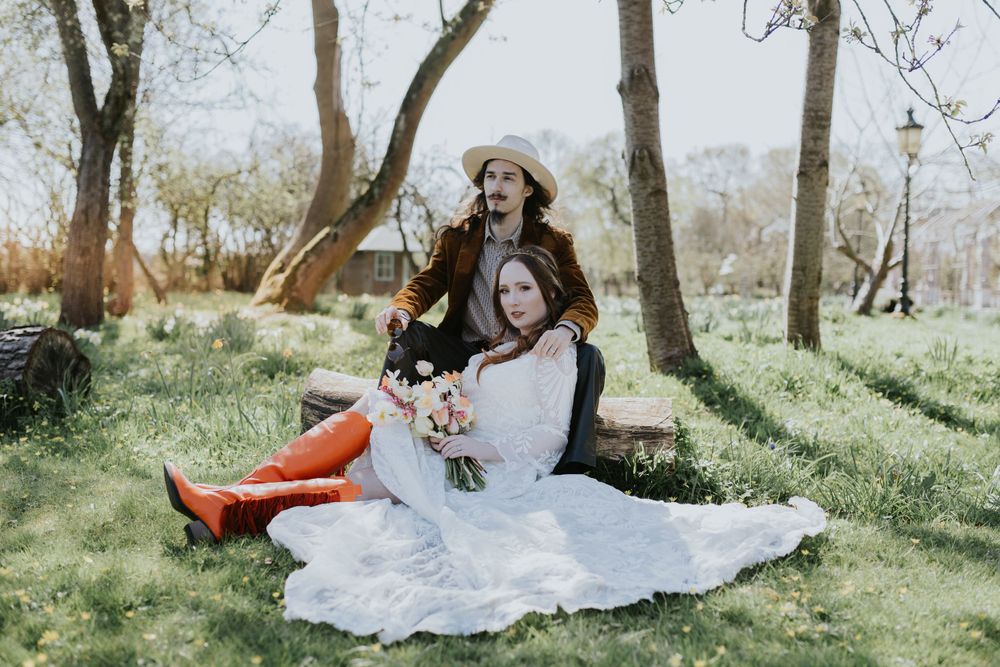 A couple sits together on a blanket in a sunlit spring forest clearing during an outdoor photoshoot.