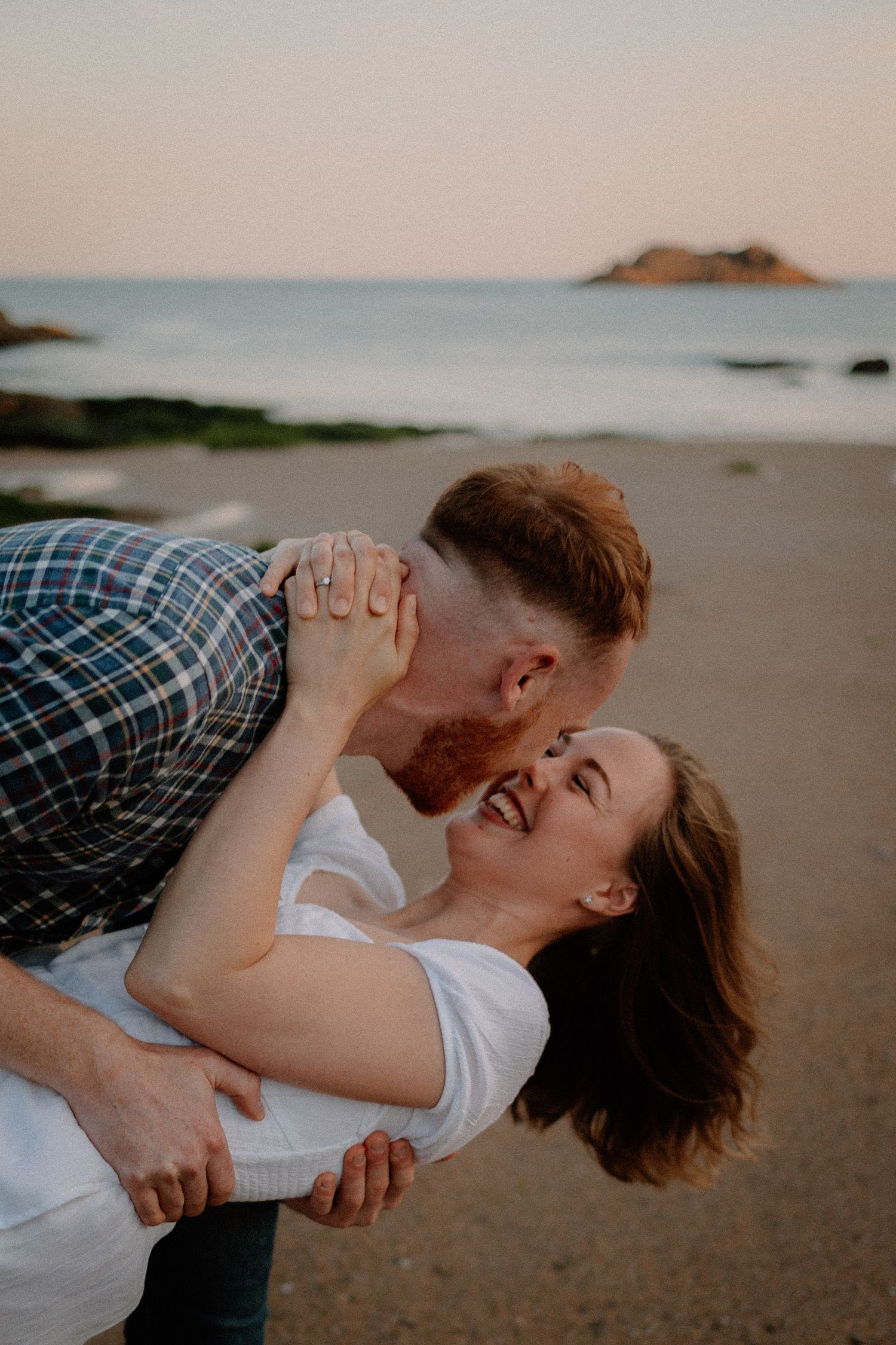 A playful couple shares a romantic moment on a beach at sunset.