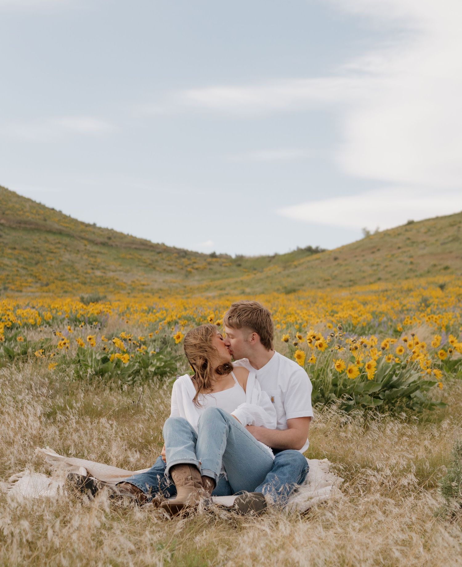 A couple relaxes in a field of vibrant orange wildflowers on a sunny afternoon in the countryside.