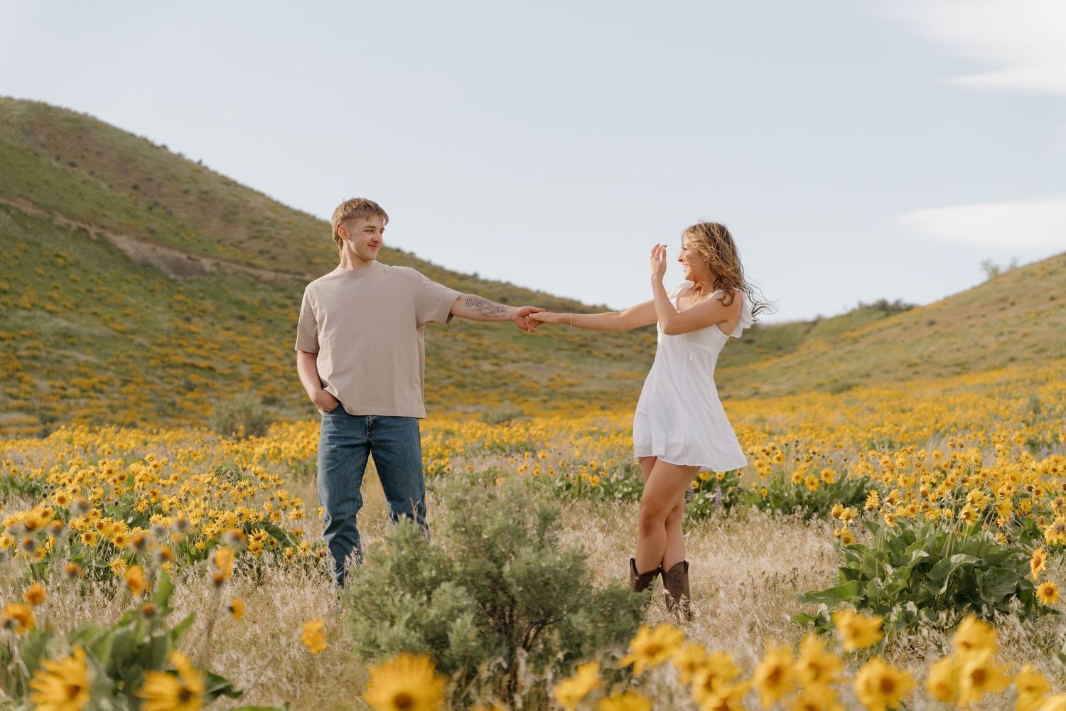 Couple walking through vibrant yellow wildflower field on sunny hillside during golden hour.