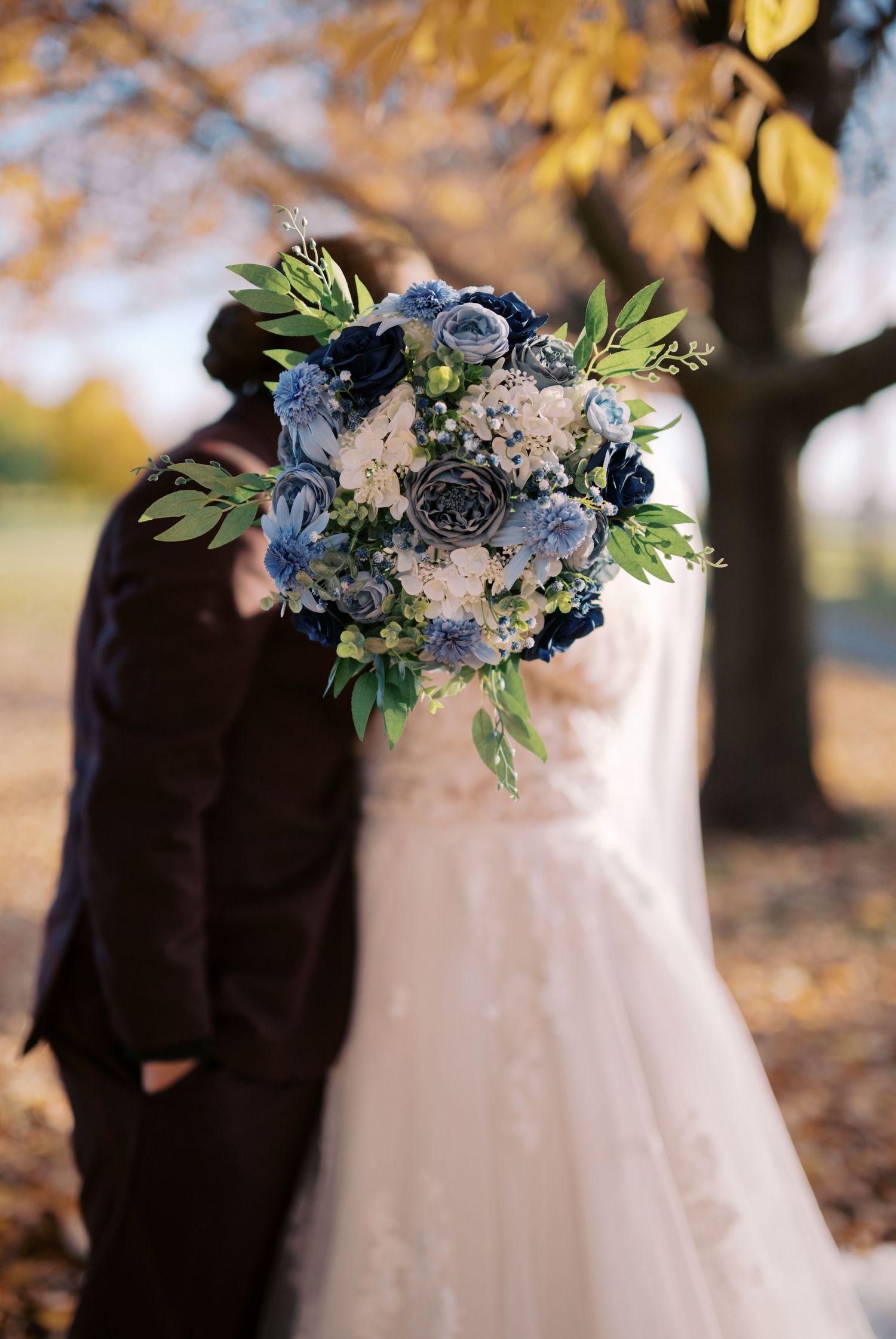 A beautiful blue and white wedding bouquet featuring delicate flowers and greenery against a warm autumn backdrop.