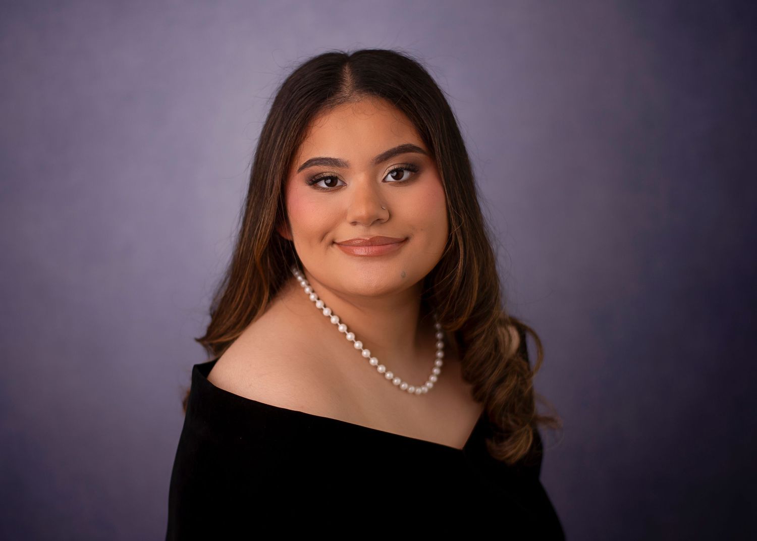 Elegant portrait against purple background featuring pearl necklace and black top.