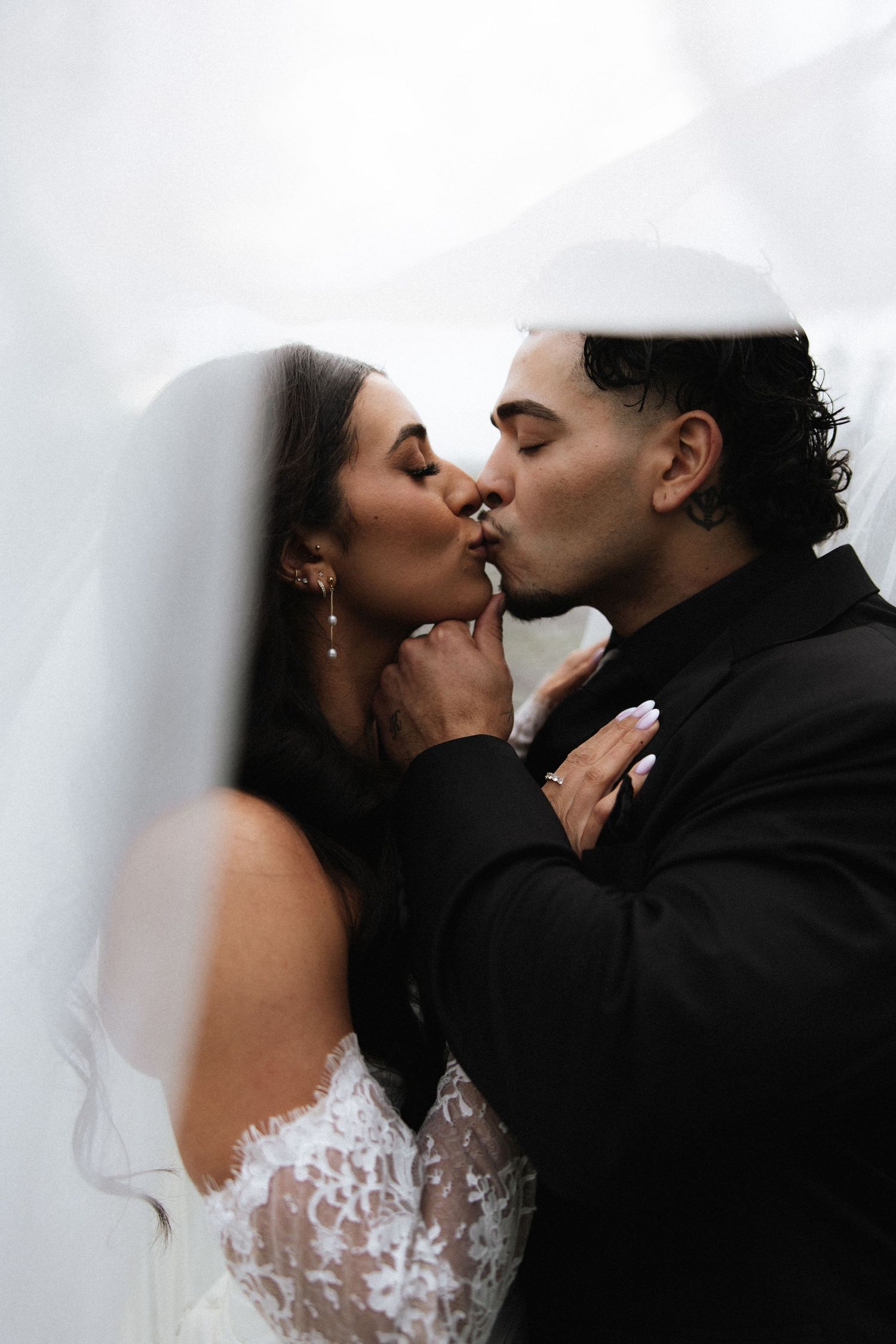 A couple shares a romantic moment under a clear umbrella surrounded by pink flowers and greenery on their wedding day. PA photographer