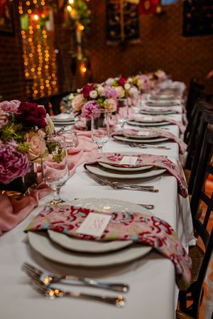 Elegant table setting with pink floral centerpieces, white linens, and decorative paisley napkins at a formal dinner event.