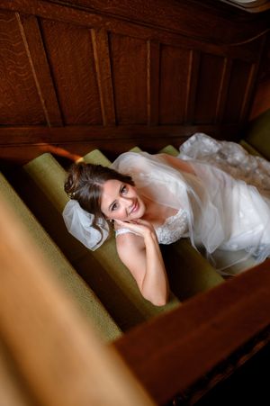 Person in flowing white wedding dress lounges on olive green couch with warm wooden wall paneling.