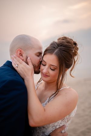 Tender moment between newlyweds embracing at sunset with bride in lace gown and groom in navy suit.
