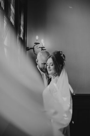 Dramatic black and white candid wedding portrait captures intimate moment between couple in soft window light.