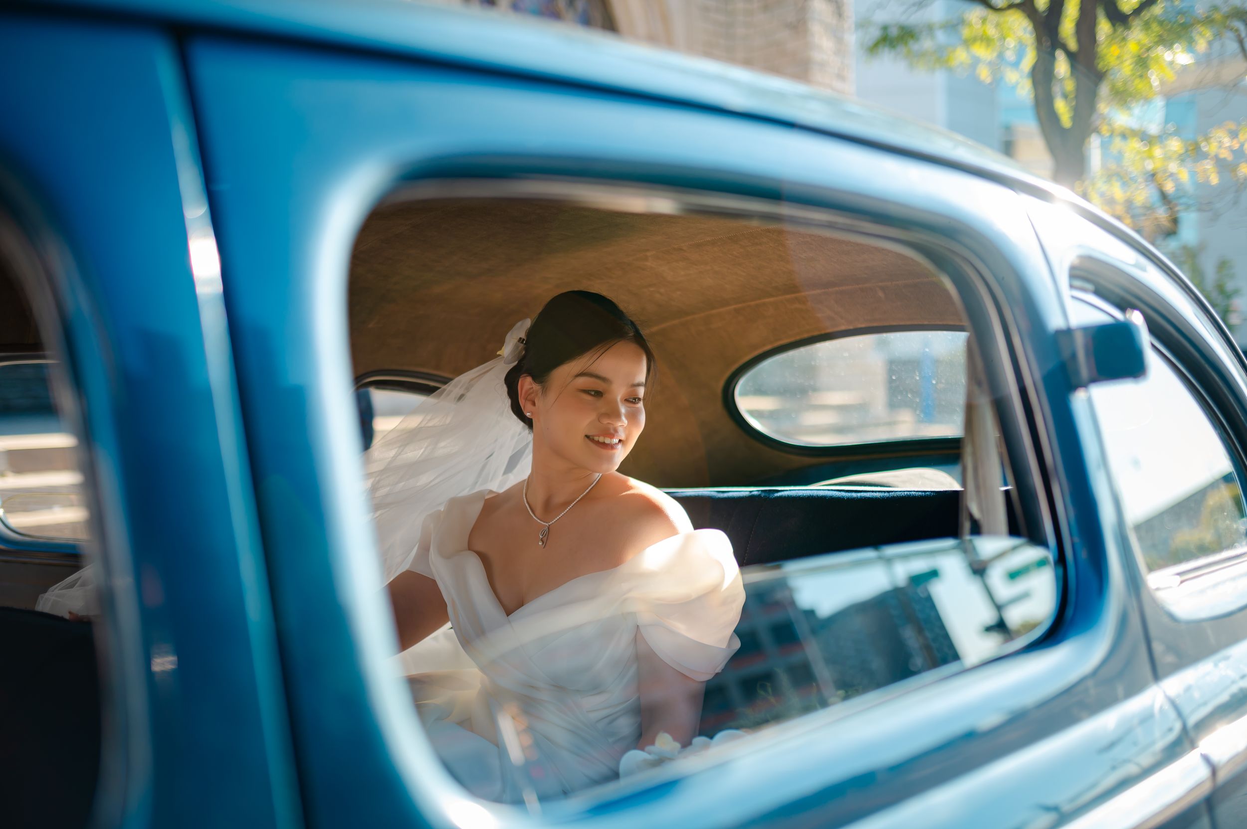 A bride in a white dress looks out the window of a classic blue vintage car during a wedding day photoshoot Detroit Bride
