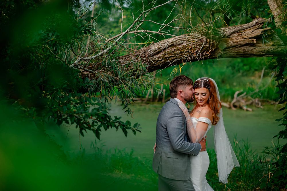 A couple shares a romantic moment by a lake surrounded by lush greenery and overhanging branches Michigan Wedding