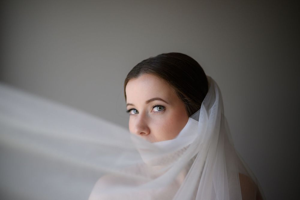 Bride draped elegantly in veil fabric stands in ethereal light creating a dreamlike bridal portrait Grand Rapids Michigan Wedding