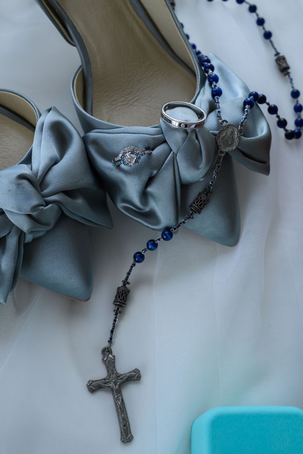 Close-up view of a rosary with blue beads and silver crucifix lying beside tiffany & co wedding ring box