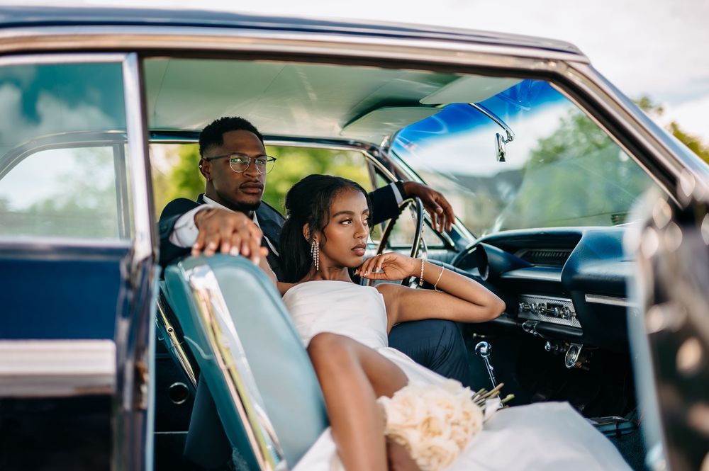People sitting in vintage car with leather interior on sunny day during outdoor photoshoot.